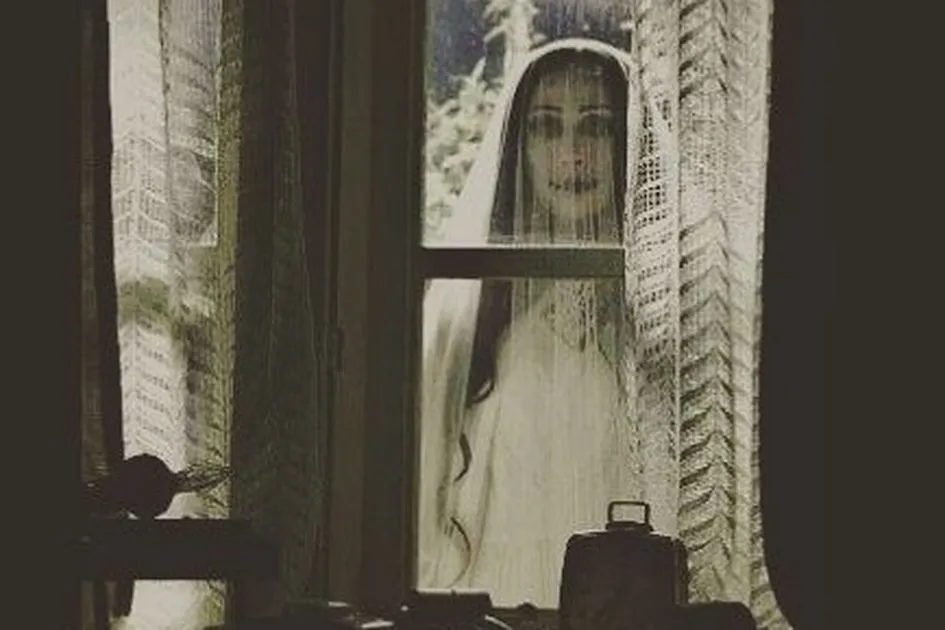 Pengabdi Setan - A woman standing outside the window waering white dress and white veil with scary face
